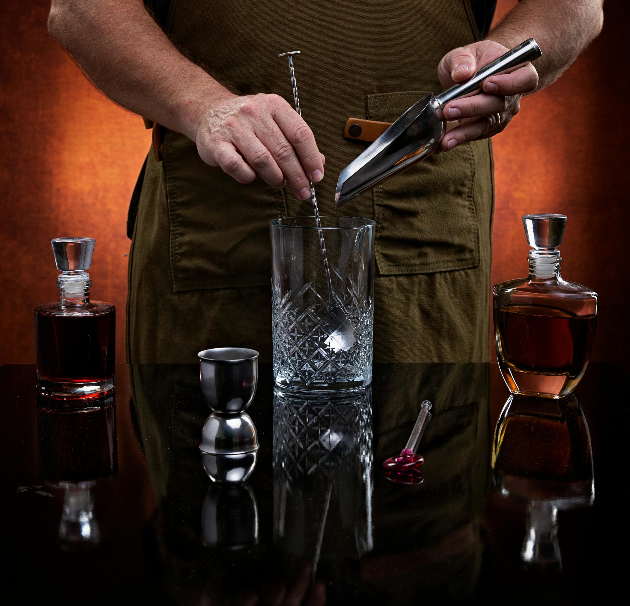 Close-up of a bartender mixing a cocktail with tools and ingredients on display.