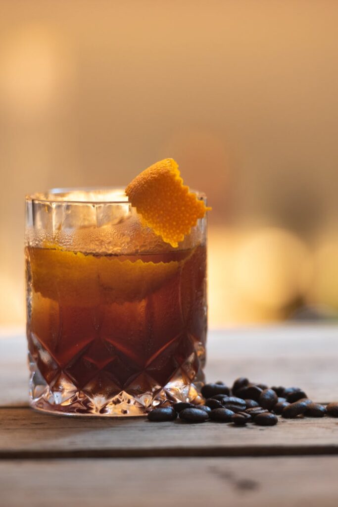 Close-up of a cocktail with orange peel and coffee beans on a rustic table.