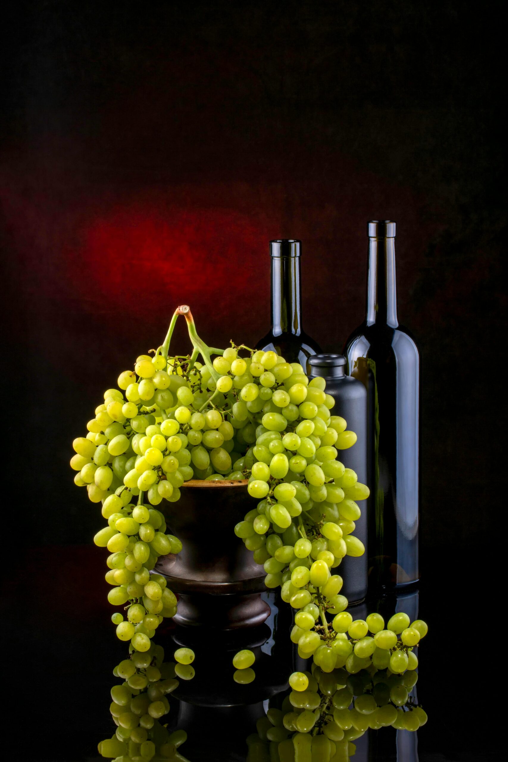 A classic still life showcasing vibrant green grapes cascading from a bowl next to elegant wine bottles.